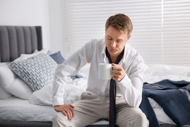Photo of Sad young man with cup of coffee getting ready at home