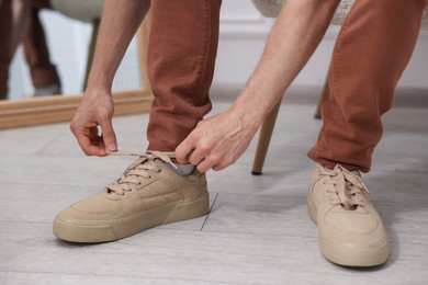 Photo of Getting ready. Young man putting on stylish shoes at home, closeup