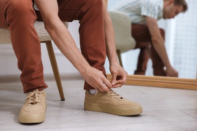 Photo of Getting ready. Young man putting on stylish shoes at home, closeup