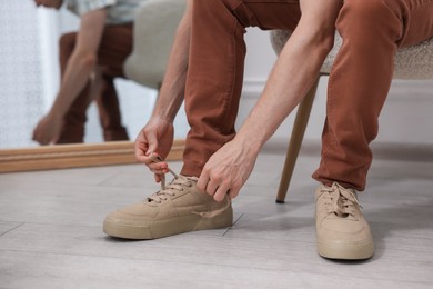 Photo of Getting ready. Young man putting on stylish shoes at home, closeup