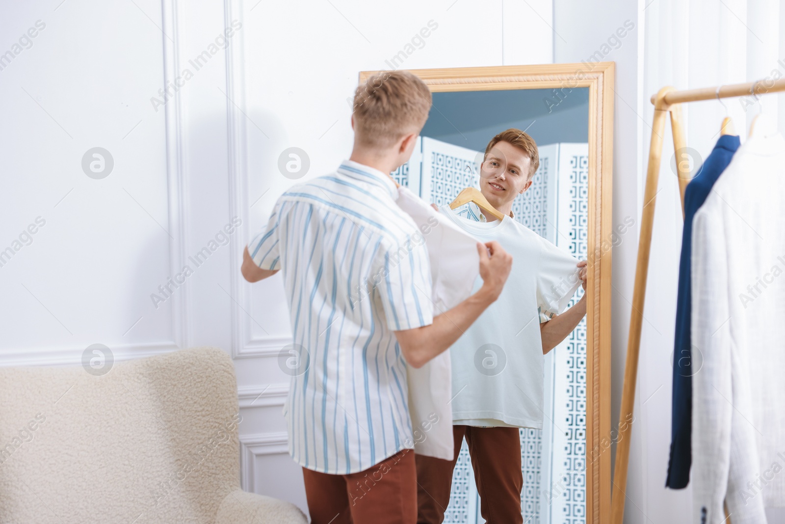 Photo of Getting ready. Young man trying on clothes near mirror at home