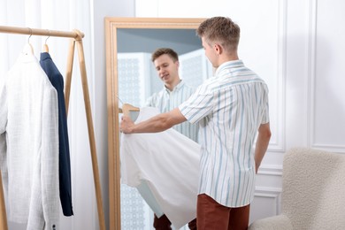 Photo of Getting ready. Young man trying on clothes near mirror at home