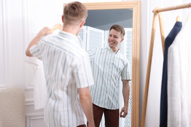 Photo of Getting ready. Young man trying on clothes near mirror at home