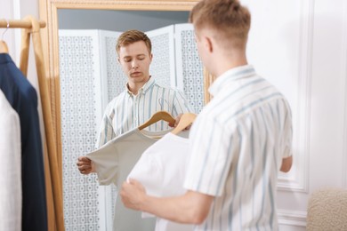 Photo of Getting ready. Young man trying on clothes near mirror at home