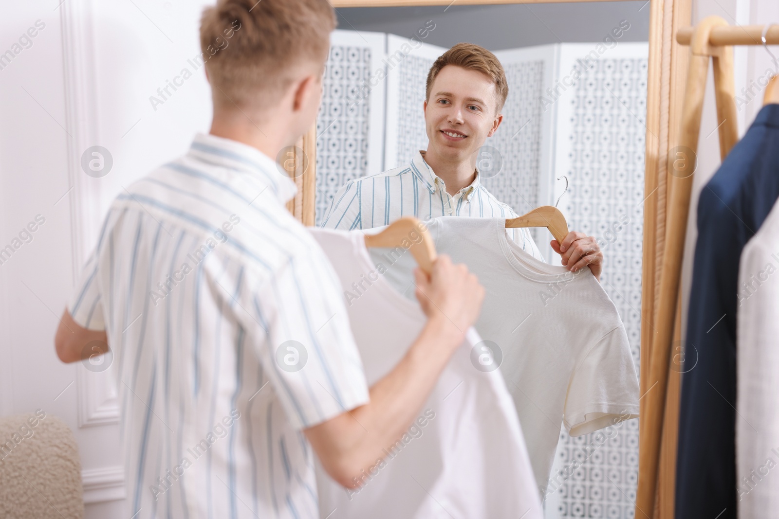 Photo of Getting ready. Young man trying on clothes near mirror at home