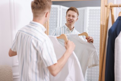 Photo of Getting ready. Young man trying on clothes near mirror at home
