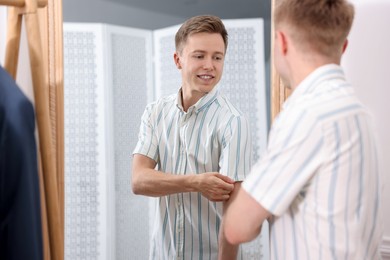 Photo of Getting ready. Young man trying on clothes near mirror at home