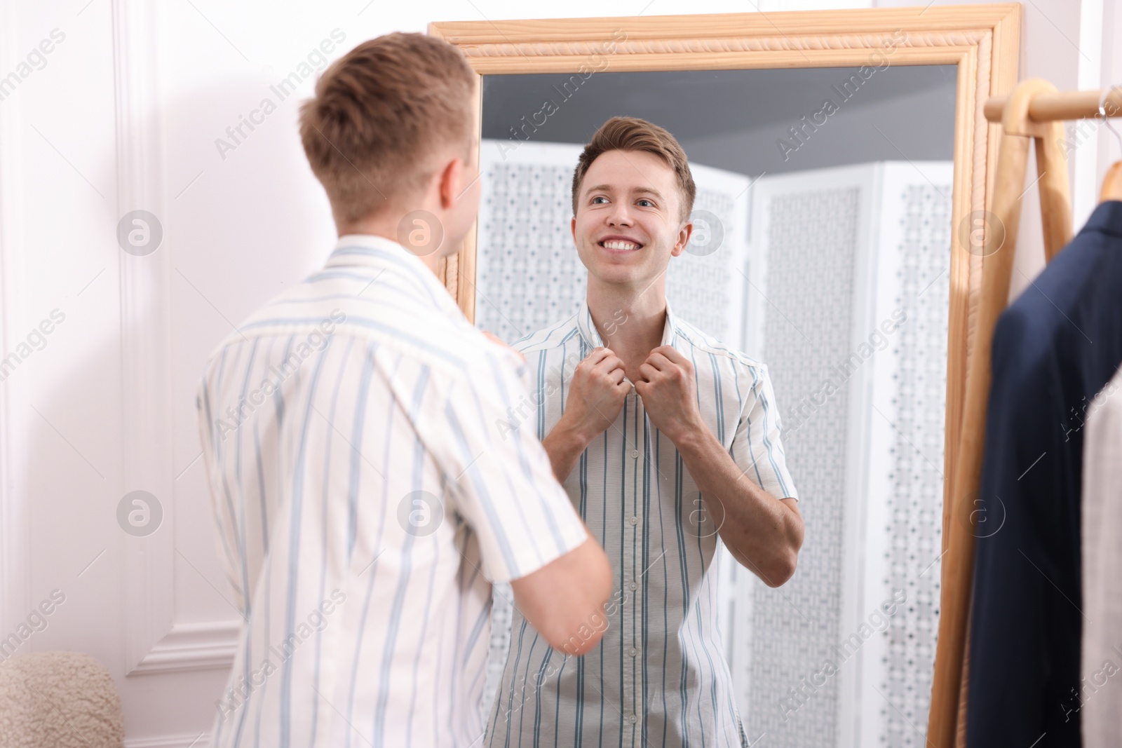 Getting ready. Young man trying on clothes near mirror at home Photo of Getting ready. Young man trying on clothes near mirror at home