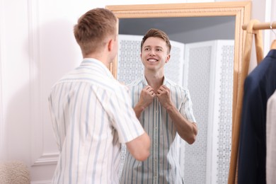 Photo of Getting ready. Young man trying on clothes near mirror at home