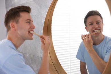 Photo of Getting ready. Young man brushing his teeth near mirror at home