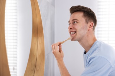 Photo of Getting ready. Young man brushing his teeth near mirror at home