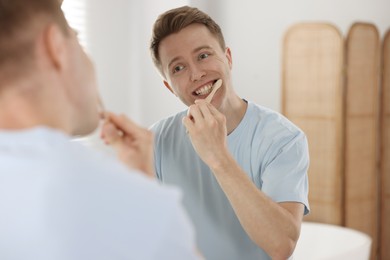 Photo of Getting ready. Young man brushing his teeth near mirror at home
