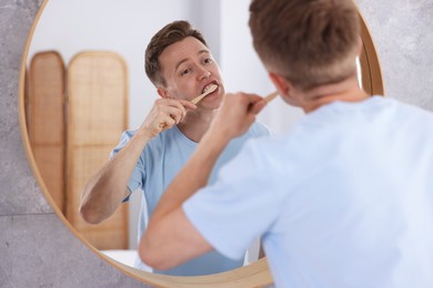 Photo of Getting ready. Young man brushing his teeth near mirror at home