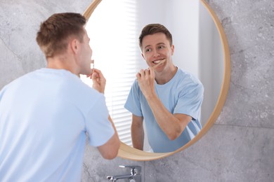 Photo of Getting ready. Young man brushing his teeth near mirror at home