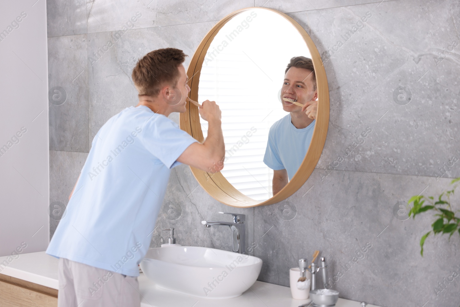 Photo of Getting ready. Young man brushing his teeth near mirror at home