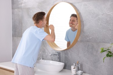 Photo of Getting ready. Young man brushing his teeth near mirror at home