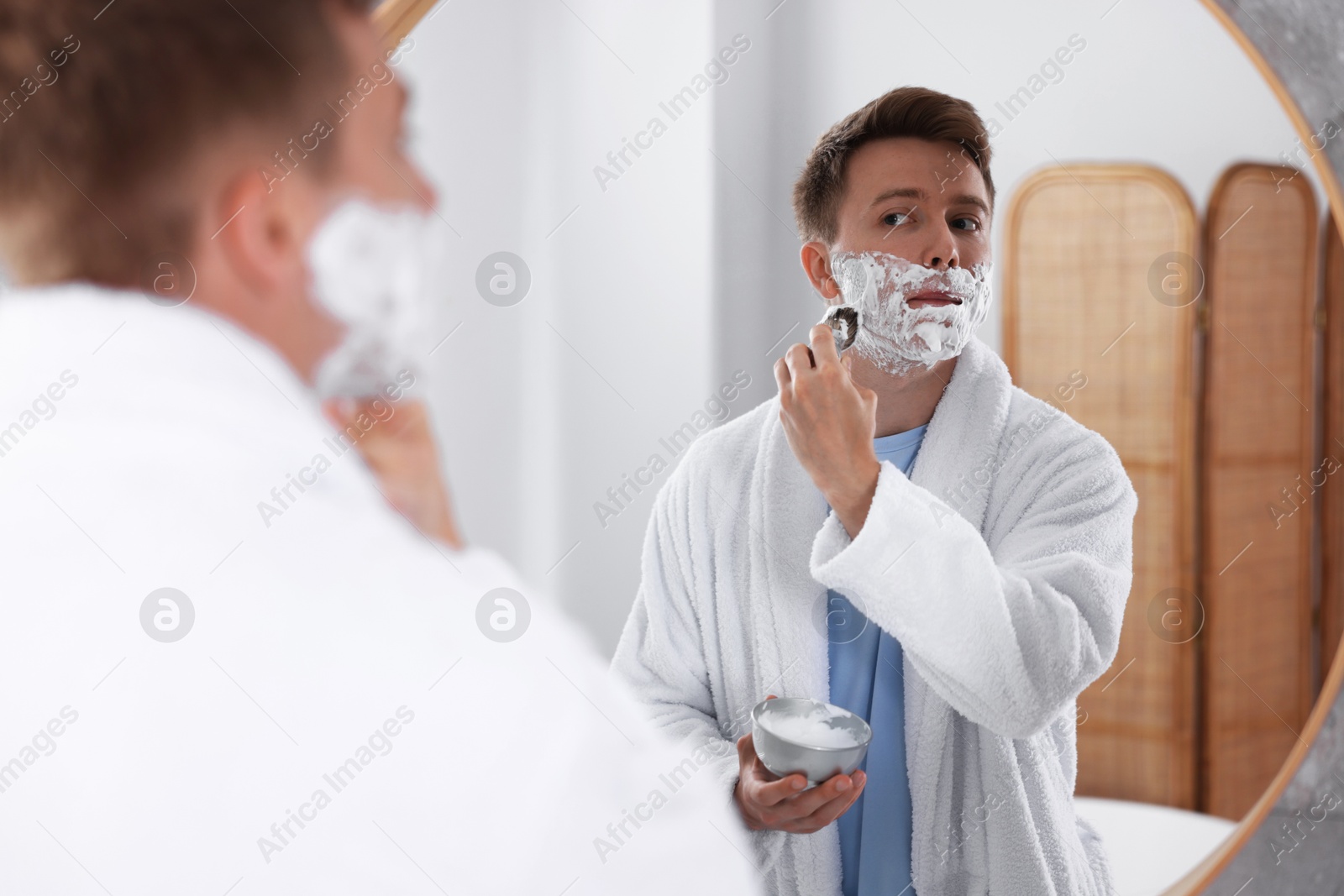 Getting ready. Young man shaving with cream near mirror at home Photo of Getting ready. Young man shaving with cream near mirror at home