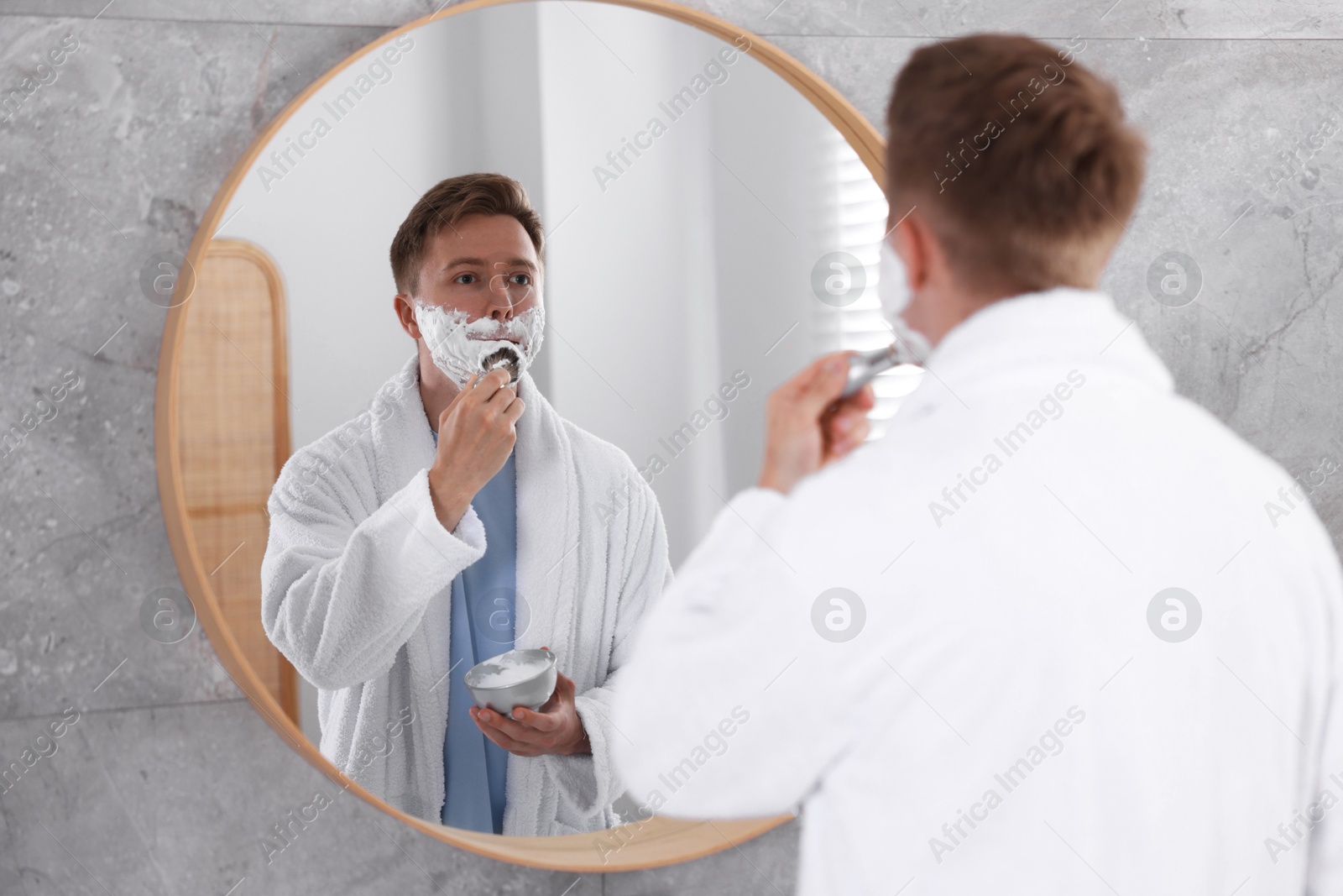 Getting ready. Young man shaving with cream near mirror at home Photo of Getting ready. Young man shaving with cream near mirror at home