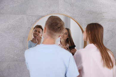 Photo of Young couple getting ready together near mirror at home