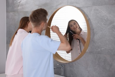 Photo of Young couple getting ready together near mirror at home