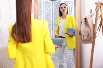Photo of Getting ready. Young woman trying on clothes near mirror at home
