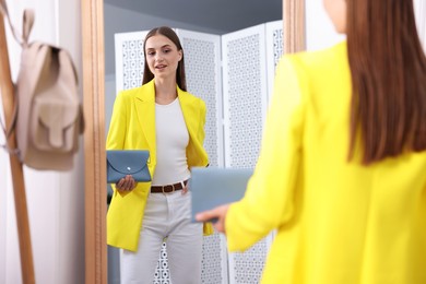 Photo of Getting ready. Young woman trying on clothes near mirror at home