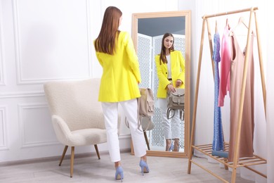 Photo of Getting ready. Young woman trying on clothes near mirror at home