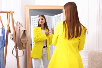 Photo of Getting ready. Young woman trying on clothes near mirror at home