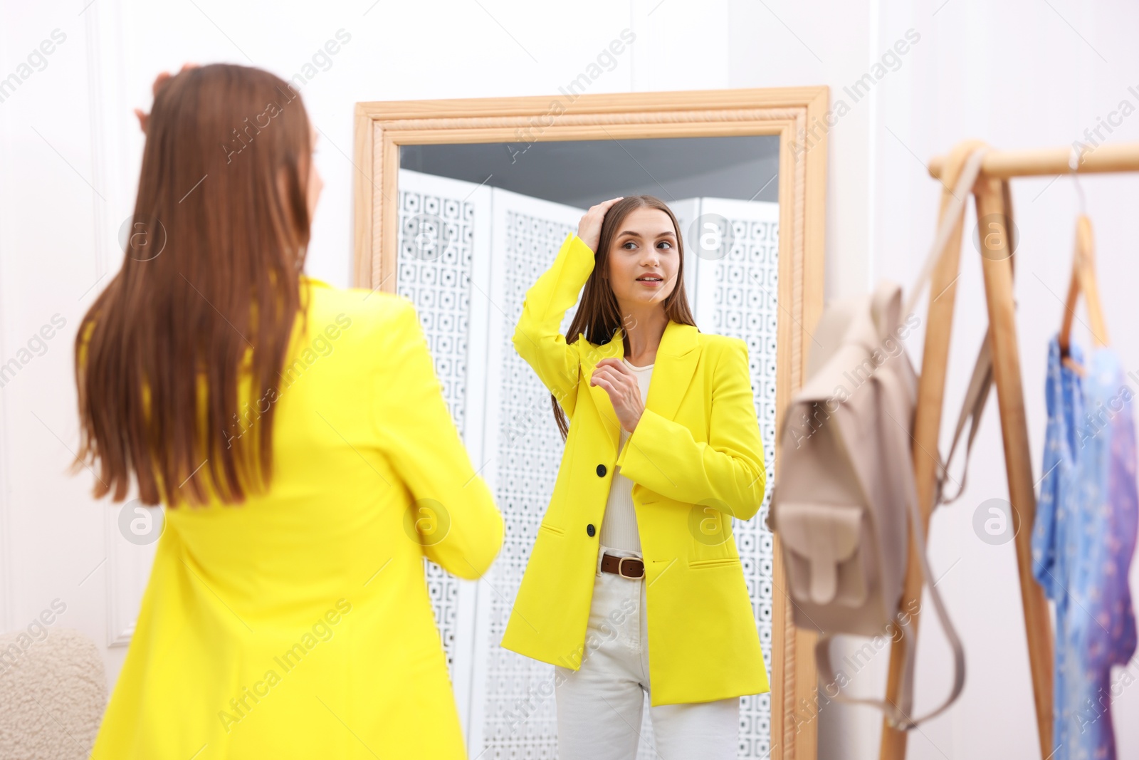 Photo of Getting ready. Young woman trying on clothes near mirror at home