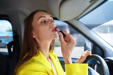 Photo of Getting ready. Young woman applying lipstick in car