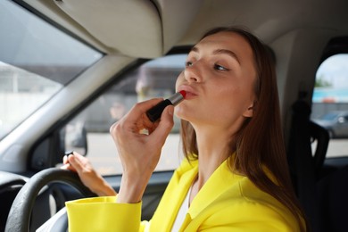 Photo of Getting ready. Young woman applying lipstick in car