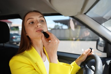 Photo of Getting ready. Young woman applying lipstick in car