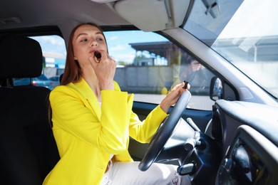 Photo of Getting ready. Young woman applying lipstick in car