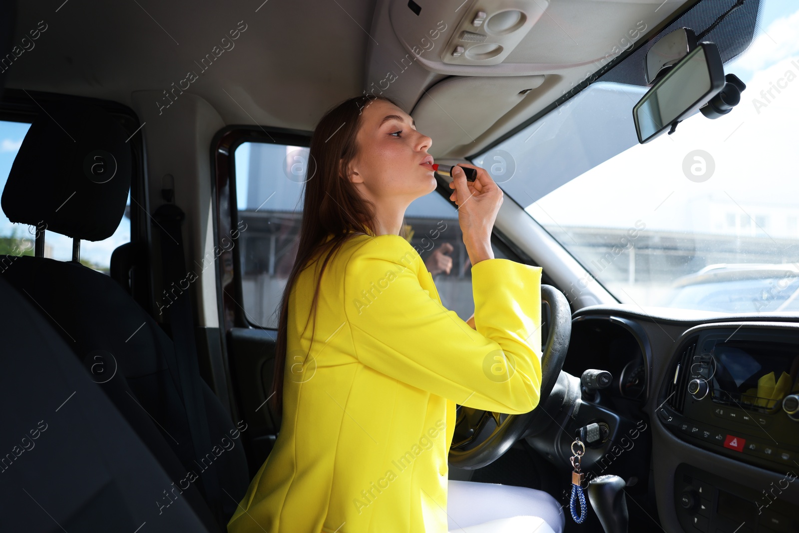 Photo of Getting ready. Young woman applying lipstick in car
