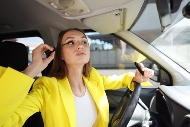 Photo of Getting ready. Young woman applying mascara in car