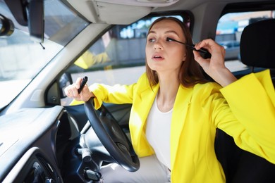 Photo of Getting ready. Young woman applying mascara in car