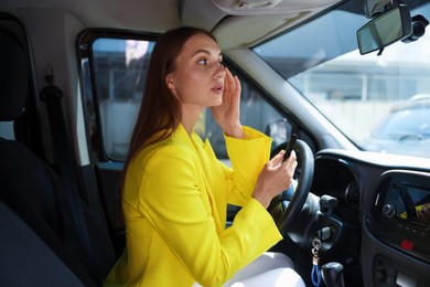Photo of Getting ready. Young woman looking at mirror in car