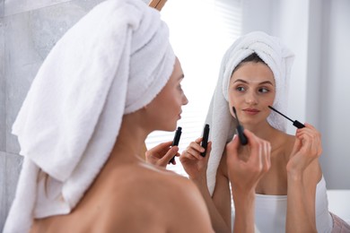 Photo of Getting ready. Young woman applying mascara near mirror at home
