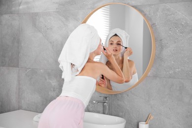 Photo of Getting ready. Young woman applying mascara near mirror at home
