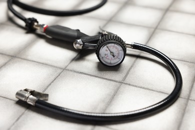Photo of One tire inflation gun with gauge on light tiled background, closeup