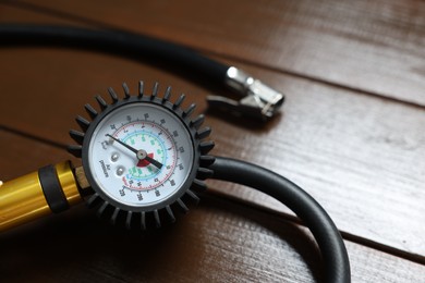 Photo of One tire inflation gun with gauge on wooden background, closeup