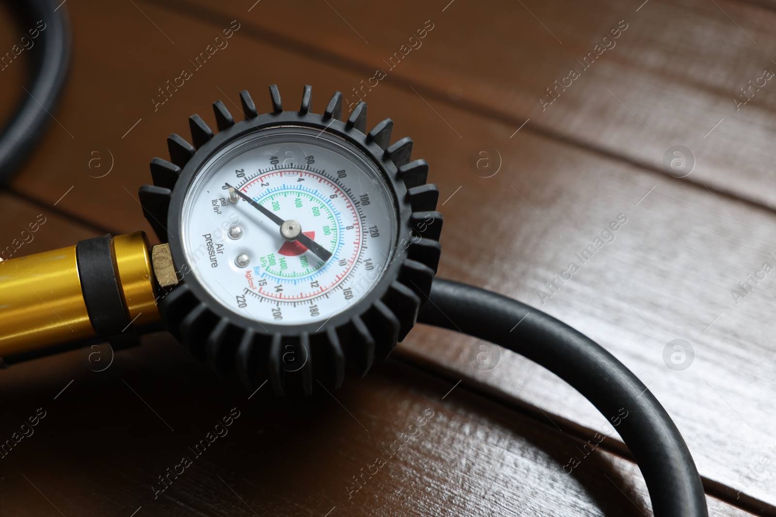 Photo of One tire inflation gun with gauge on wooden background, closeup