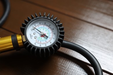Photo of One tire inflation gun with gauge on wooden background, closeup
