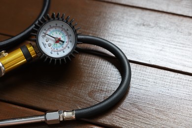 Photo of One tire inflation gun with gauge on wooden background, closeup