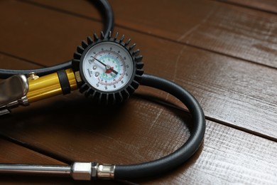 Photo of One tire inflation gun with gauge on wooden background, closeup