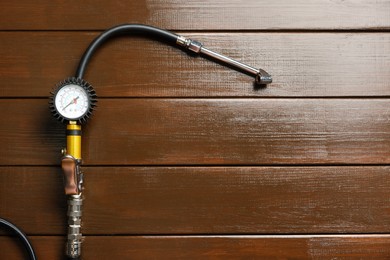 Photo of One tire inflation gun with gauge on wooden background, top view. Space for text