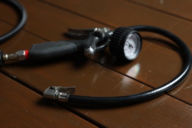 Photo of One tire inflation gun with gauge on wooden background, closeup