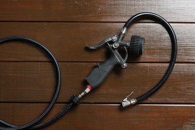 Photo of One tire inflation gun with gauge on wooden background, top view