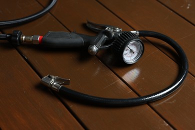 Photo of One tire inflation gun with gauge on wooden background, closeup
