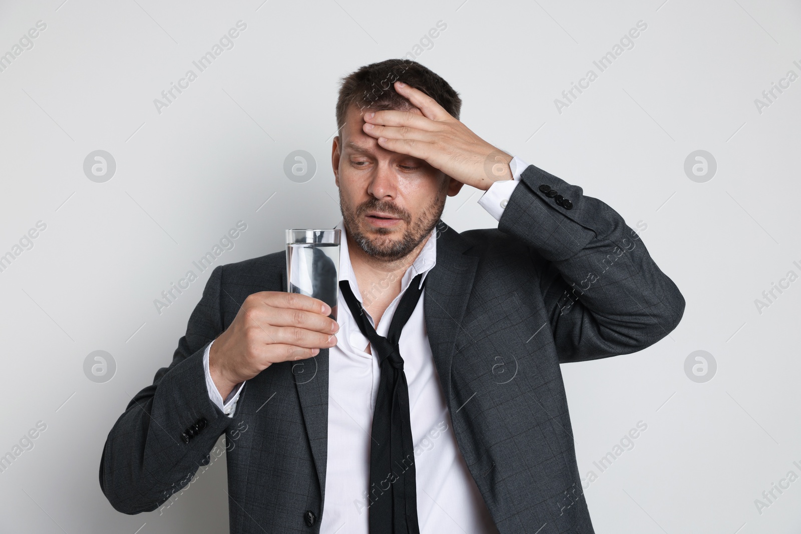 Photo of Man with glass of water suffering from hangover on white background